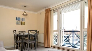 Un coin repas avec une table et des chaises, un radiateur et une vue sur un port de plaisance, visible à travers une porte vitrée.