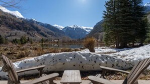 A wooden bench and table set against a mountainous backdrop with a lake and snow-covered ground.