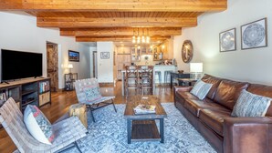 A spacious living room with a wooden ceiling, a leather sofa, a coffee table, and a TV.