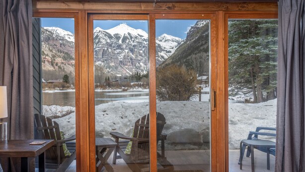 A room with a sliding glass door leading to a snowy outdoor area with chairs and a table.