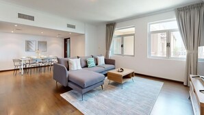 A modern living room with a grey sectional sofa, a wooden coffee table, and a dining area with a light blue table and chairs. - 605 Turia BlockA, The Greens (The Greens)