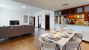 A modern living room with a sofa, dining table set for four, and a kitchen area with wooden cabinets and a built-in oven. - 605 Turia BlockA, The Greens (The Greens)