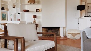 A living room with a fireplace, white furniture, and a bookshelf with decorative items. - Casa da Praia (Colares)