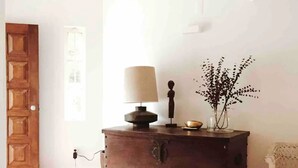 A wooden chest of drawers with a lamp and a vase with branches, a white wicker chair, and a tiled floor. - Casa da Praia (Colares)