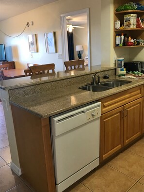 Una cocina con encimeras de granito, lavavajillas, armarios de madera y un comedor con sillas y mesa.