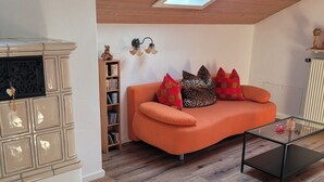 A cozy living room with a wooden ceiling, a sofa with patterned cushions, a glass coffee table, and a fireplace with a decorative cabinet. - Stilvolle Ferienwohnung im Ortszentrum, Ruhig Gelegen (Grassau)