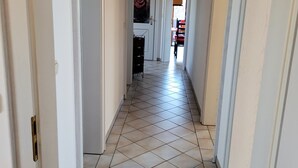 A hallway with tiled flooring and white walls, leading to a room with a ceiling fan and a door with a rose decoration. - Stilvolle Ferienwohnung im Ortszentrum, Ruhig Gelegen (Grassau)