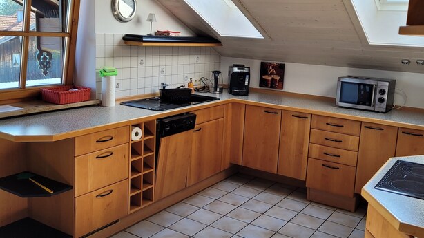 A kitchen with wooden cabinets, a tiled floor, a black stove, a microwave, and a skylight. - Stilvolle Ferienwohnung im Ortszentrum, Ruhig Gelegen (Grassau)