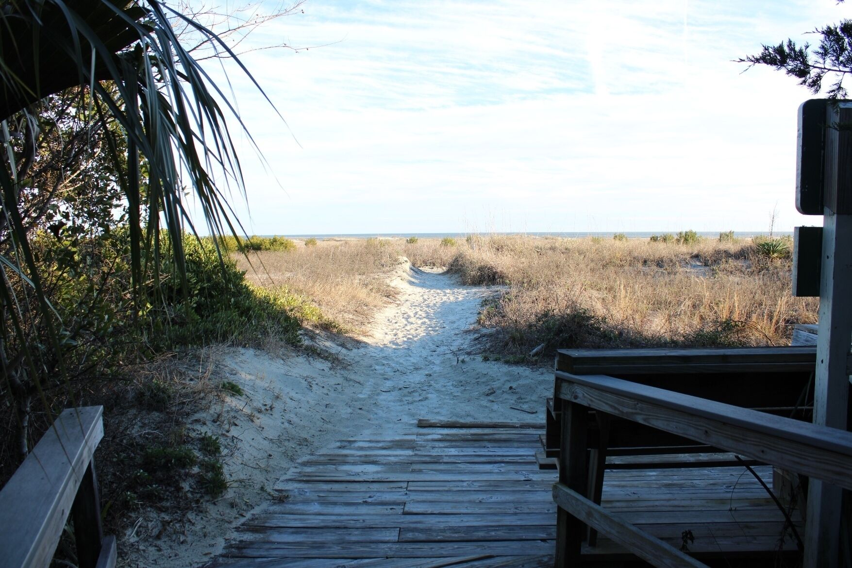 A wooden boardwalk leading to a beach with sand and sparse vegetation.