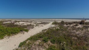 Una playa con un sendero arenoso que lleva al agua, rodeada de vegetación escasa.
