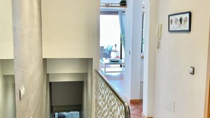Una escalera con barandilla metálica que lleva a un rellano. Hay una puerta en el rellano que da a un espacio exterior con una mesa y sillas.