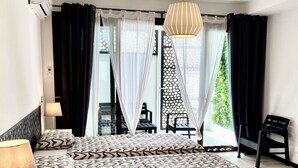 Habitación de hotel con una cama grande, una mesita de noche con lámpara, una ventana con cortinas translúcidas y vista a zonas verdes.