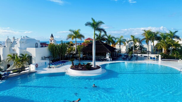 Una amplia piscina cristalina rodeada de palmeras y edificios blancos con cúpulas.