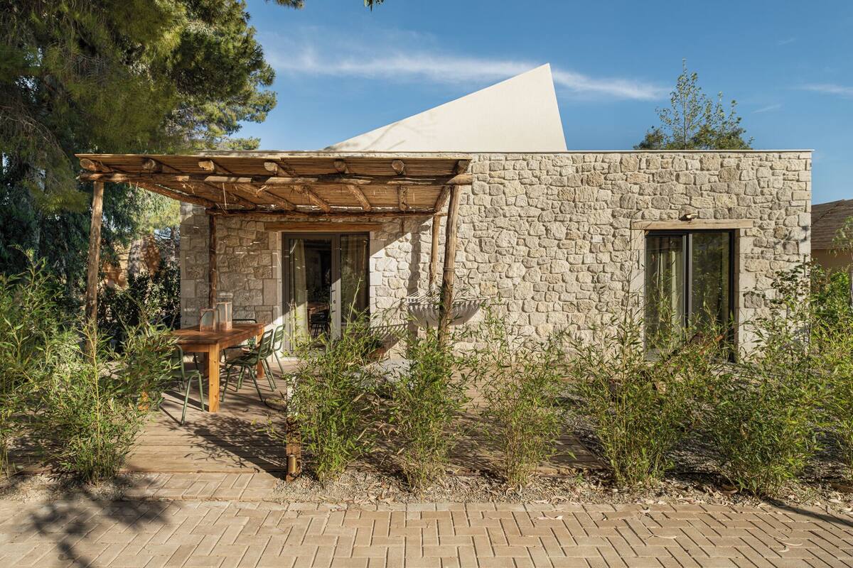 Ein Steinhaus mit einer Holzpergola, einem Tisch und Stühlen vor der Fassade.