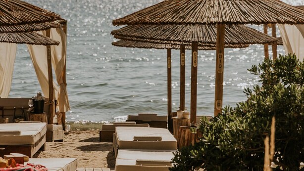 Une plage avec des parasols en chaume et des chaises longues.