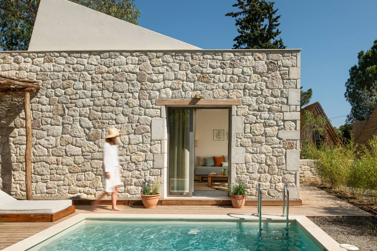 Ein modernes Gebäude aus Stein mit Pool, Holzterrasse und Topfpflanzen.