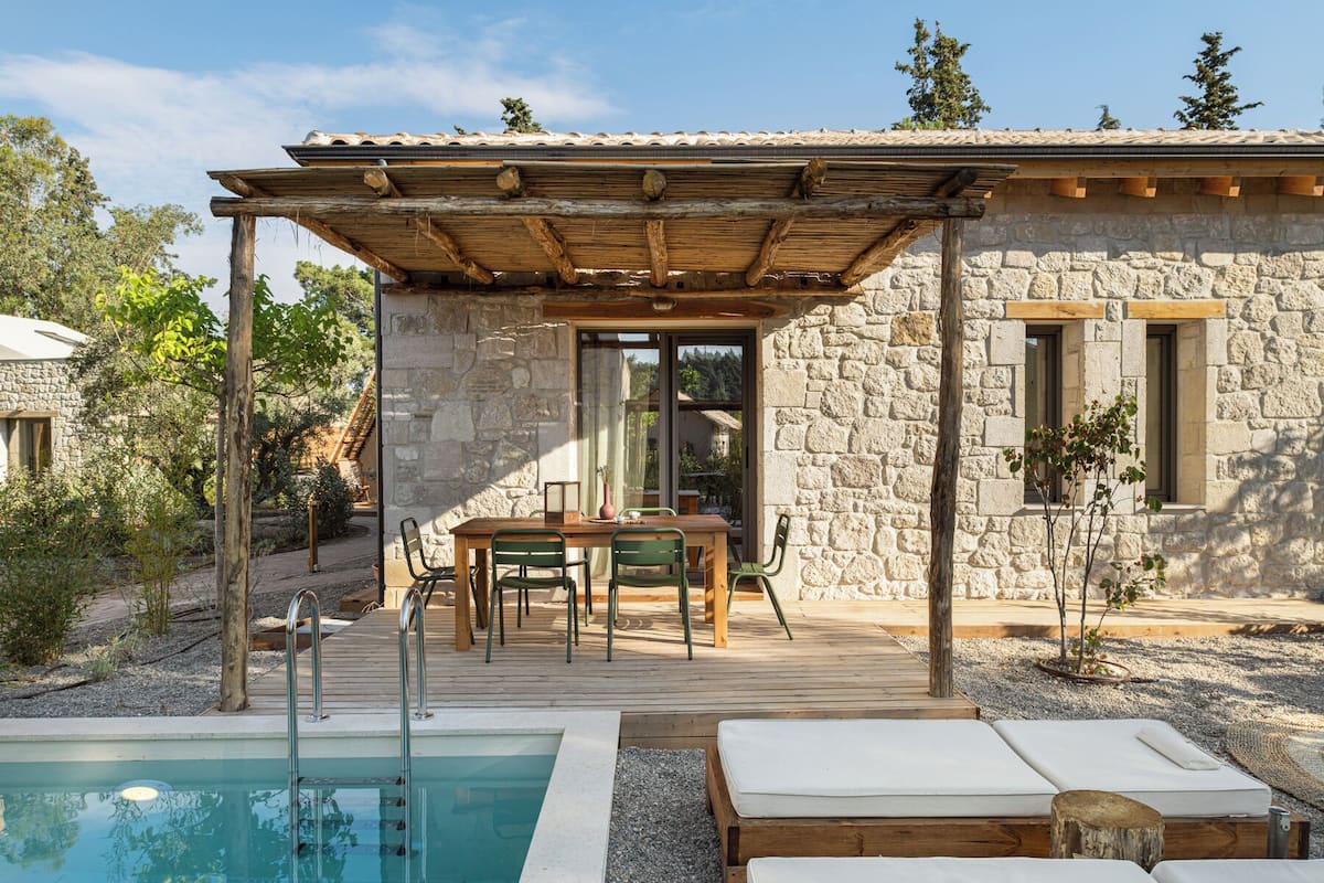 Ein Steinhaus mit einer Holzterrasse, einem Pool und Außenmöbeln.