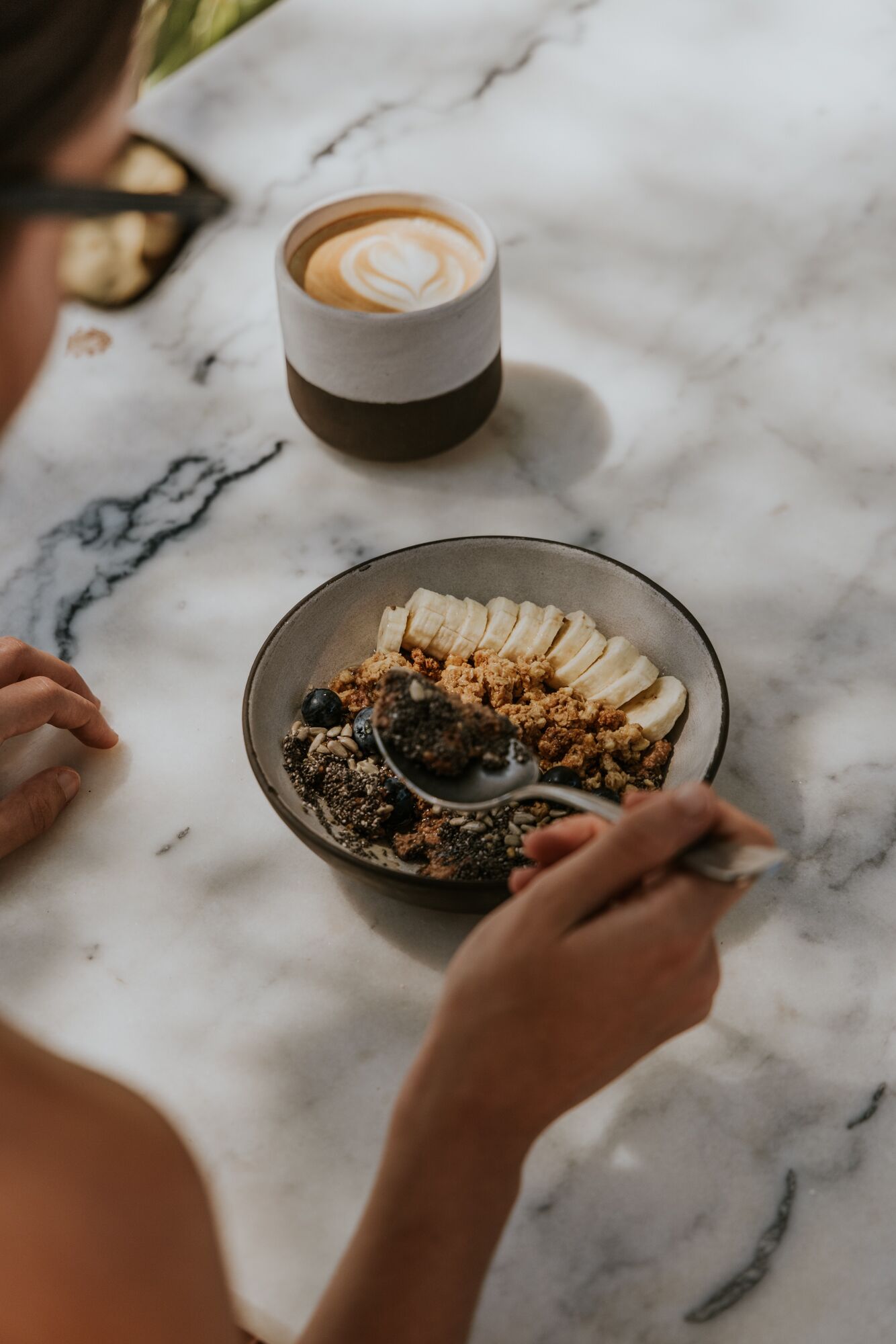 A breakfast setting with a bowl of cereal, banana slices, and a coffee cup on a marble surface.