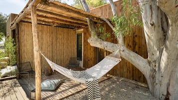 A wooden cabin with a hammock, a deck, and a tree.