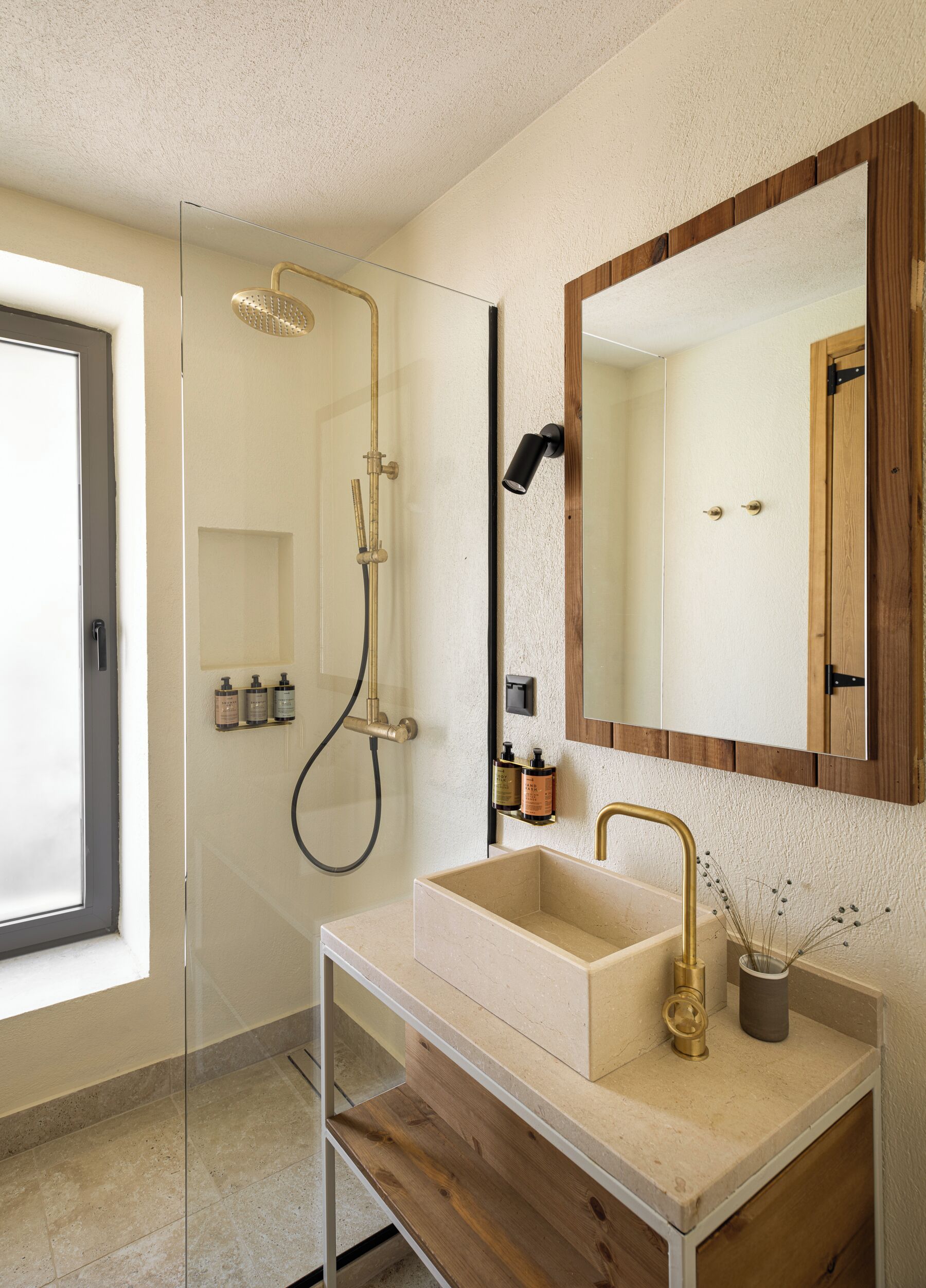 A modern bathroom with a glass-enclosed shower, a beige sink with a gold faucet, and a large mirror with a wooden frame.
