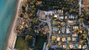 Vue aérienne d’une station balnéaire comprenant plusieurs hébergements de type bungalow, une plage et un espace piscine.
