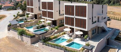Un moderno edificio de varios pisos con una zona de piscina en la azotea, múltiples piscinas y mobiliario de exterior.