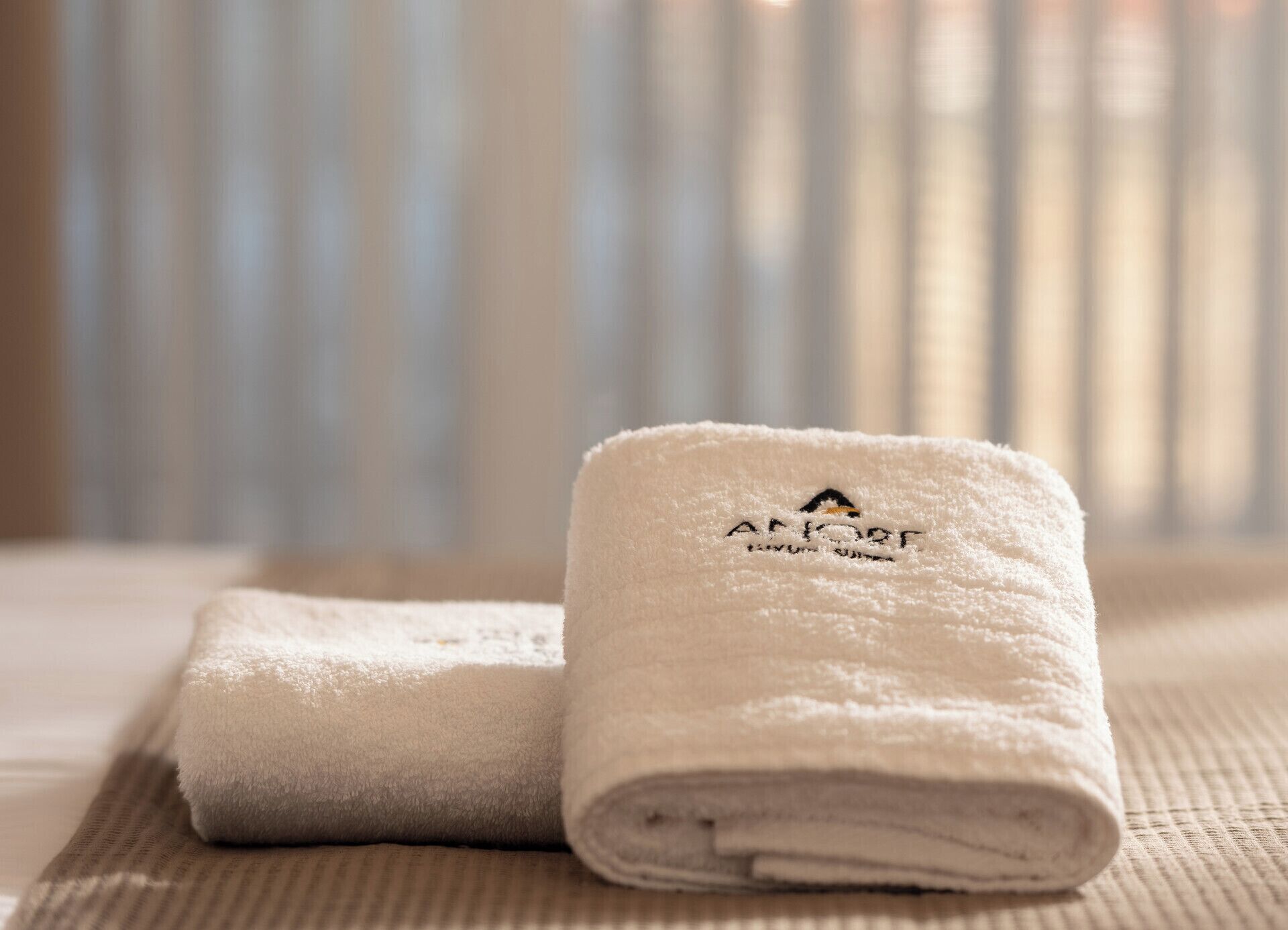 Two neatly folded white towels with a logo and text on them, placed on a textured surface.