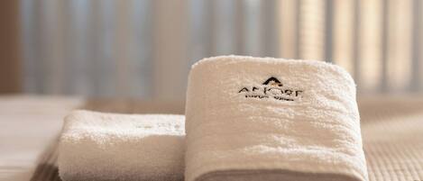 Two neatly folded white towels with a logo and text on them, placed on a textured surface.