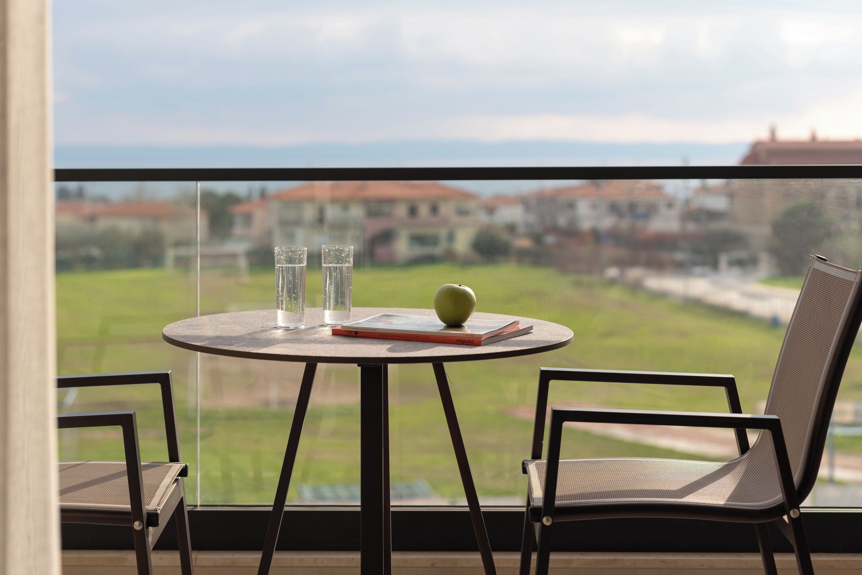 Un balcón con una mesa redonda, dos sillas, un libro y una manzana verde.