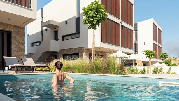 A modern hotel with a swimming pool, stone facade, and multiple balconies. - Anore Luxury Suites  (Sithonia)