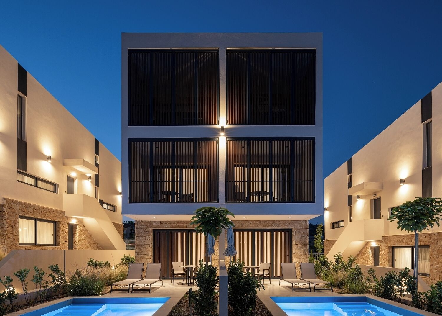 Un edificio moderno de dos pisos con área de piscina, asientos exteriores y fachada de piedra.