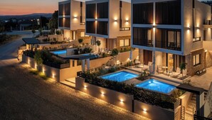 A modern multi-story building with outdoor pools and well-lit areas. - Anore Luxury Suites  (Sithonia)