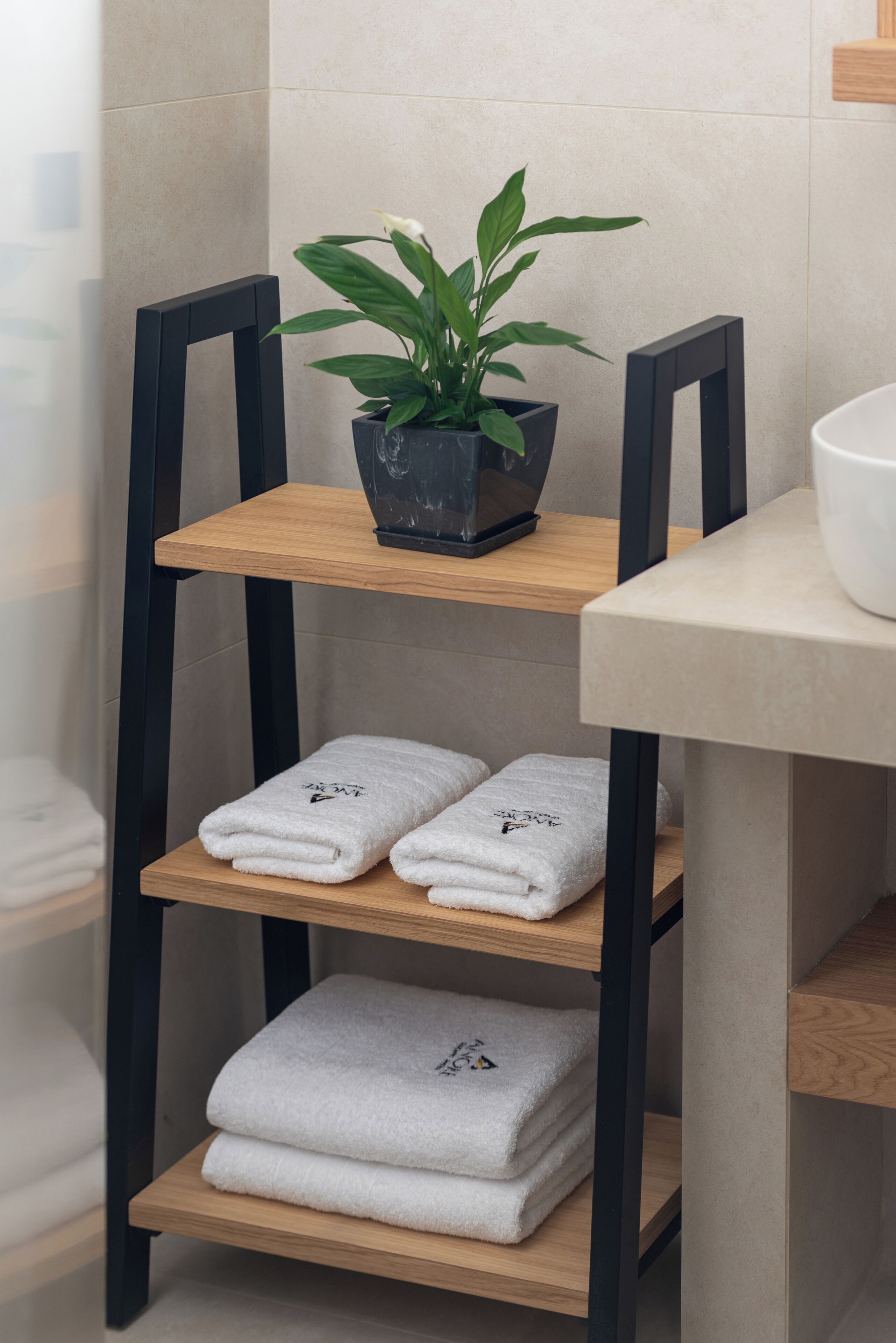 Un baño con un estante de madera que sostiene toallas y una planta en maceta.