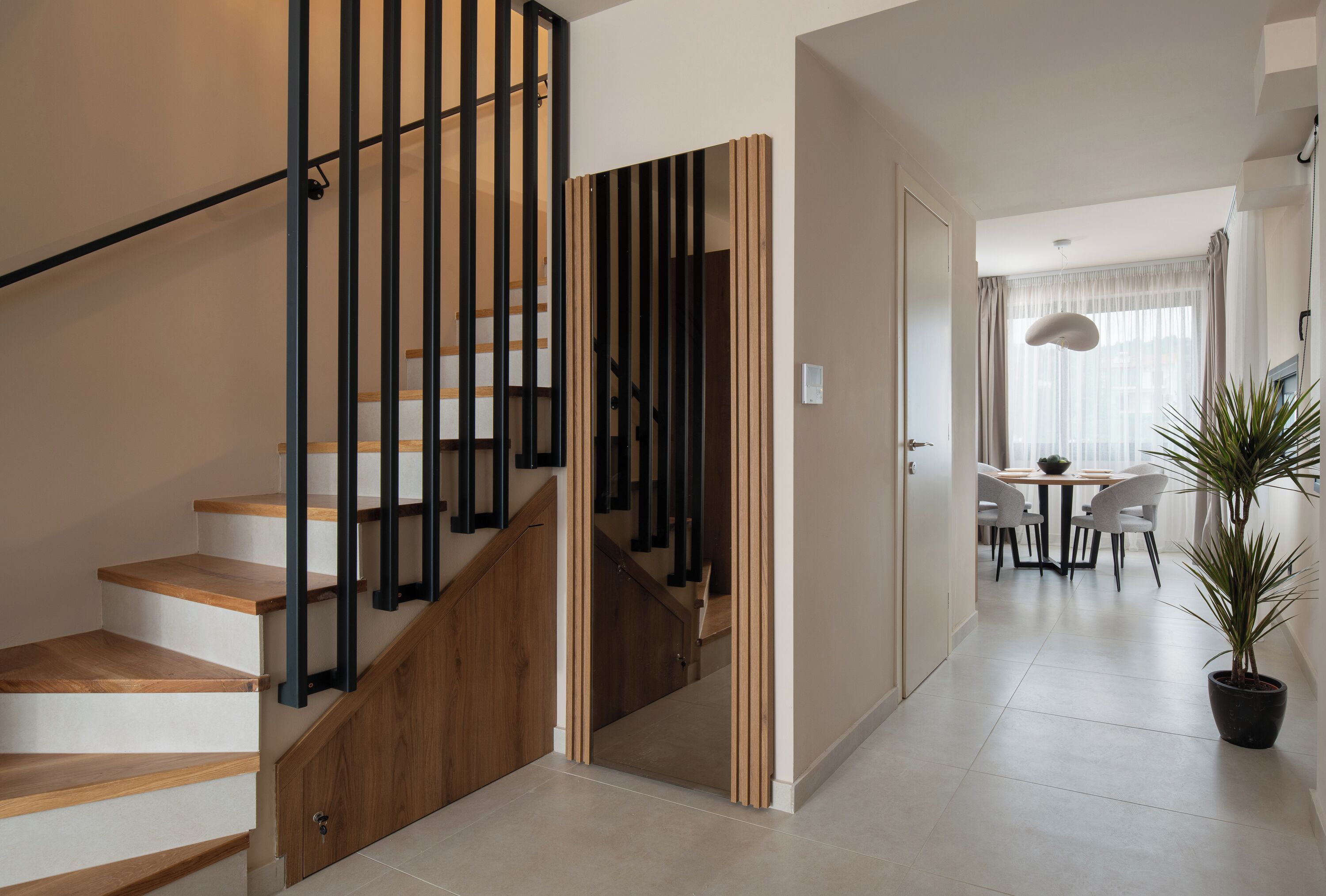 A modern staircase with wooden steps and black railings, leading to a dining area with a table and chairs.