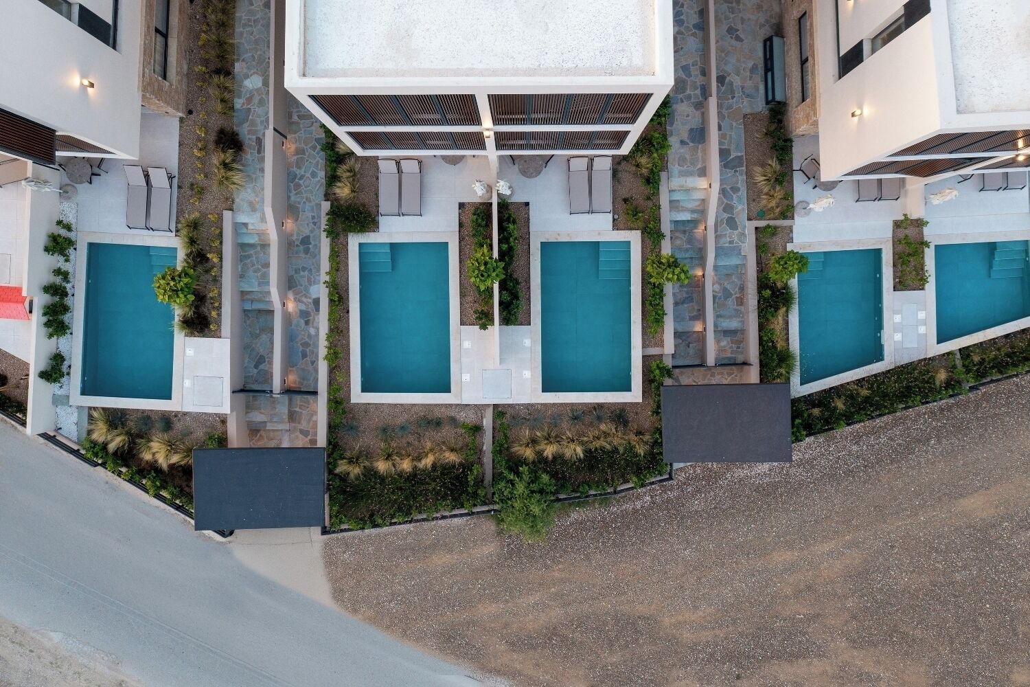 A modern building with multiple swimming pools, outdoor seating areas, and a stone pathway.