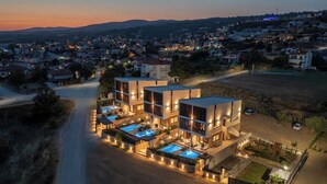 Un hotel moderno de varios pisos con una zona de piscina, rodeado de un paisaje rural.