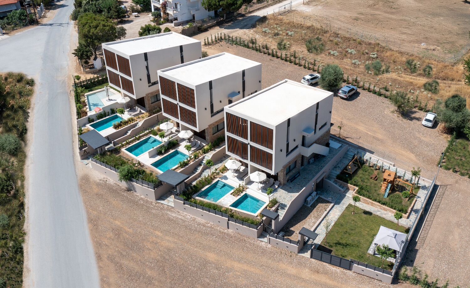 A modern multi-story building with three separate swimming pools, surrounded by a landscaped garden and a gravel driveway.