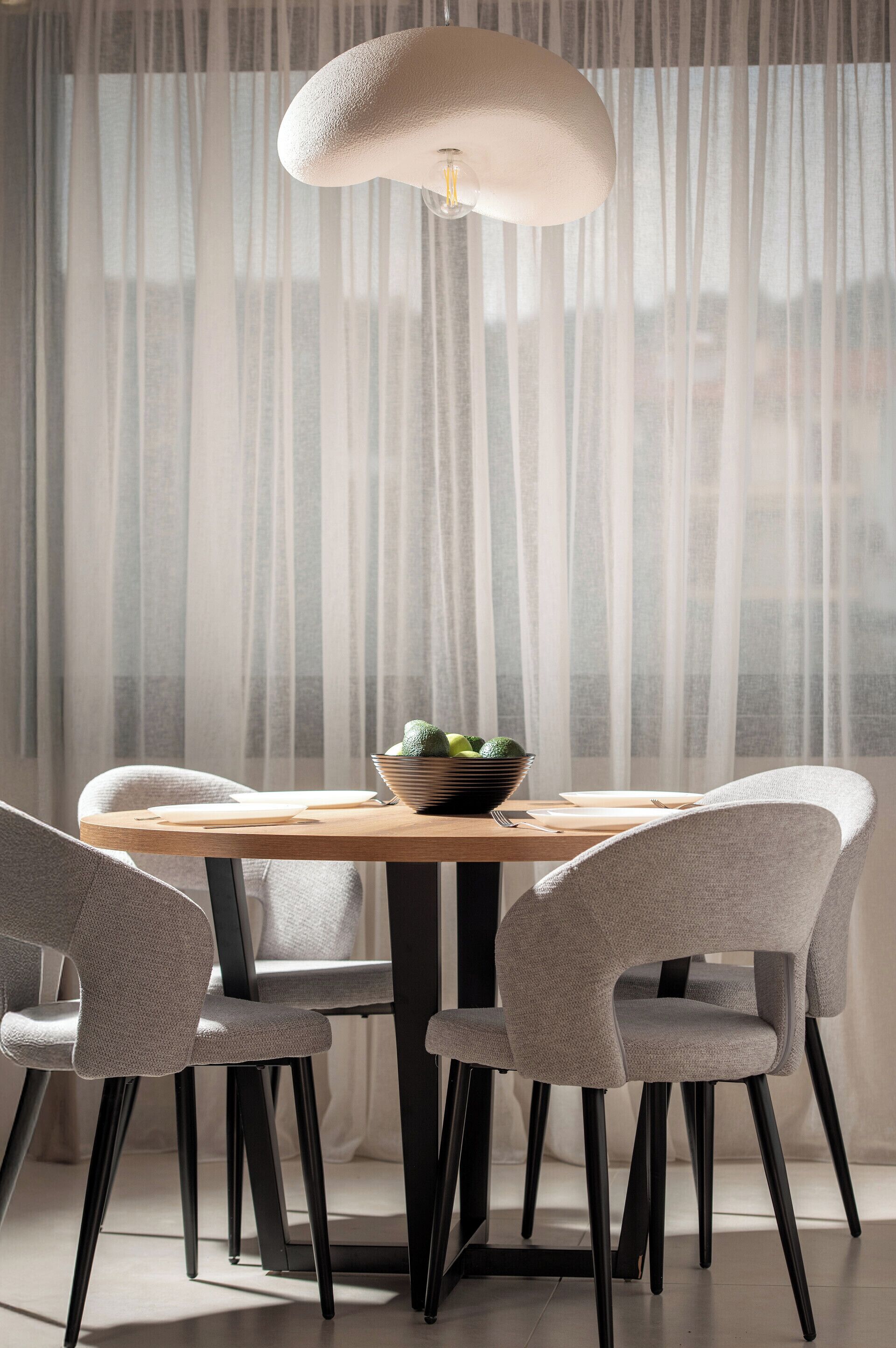 A dining area with a round table, four chairs, a bowl with a cactus, and a pendant light.