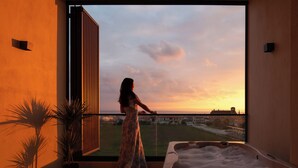 A woman standing by a large window overlooking a cityscape at sunset. - Anore Luxury Suites  (Sithonia)