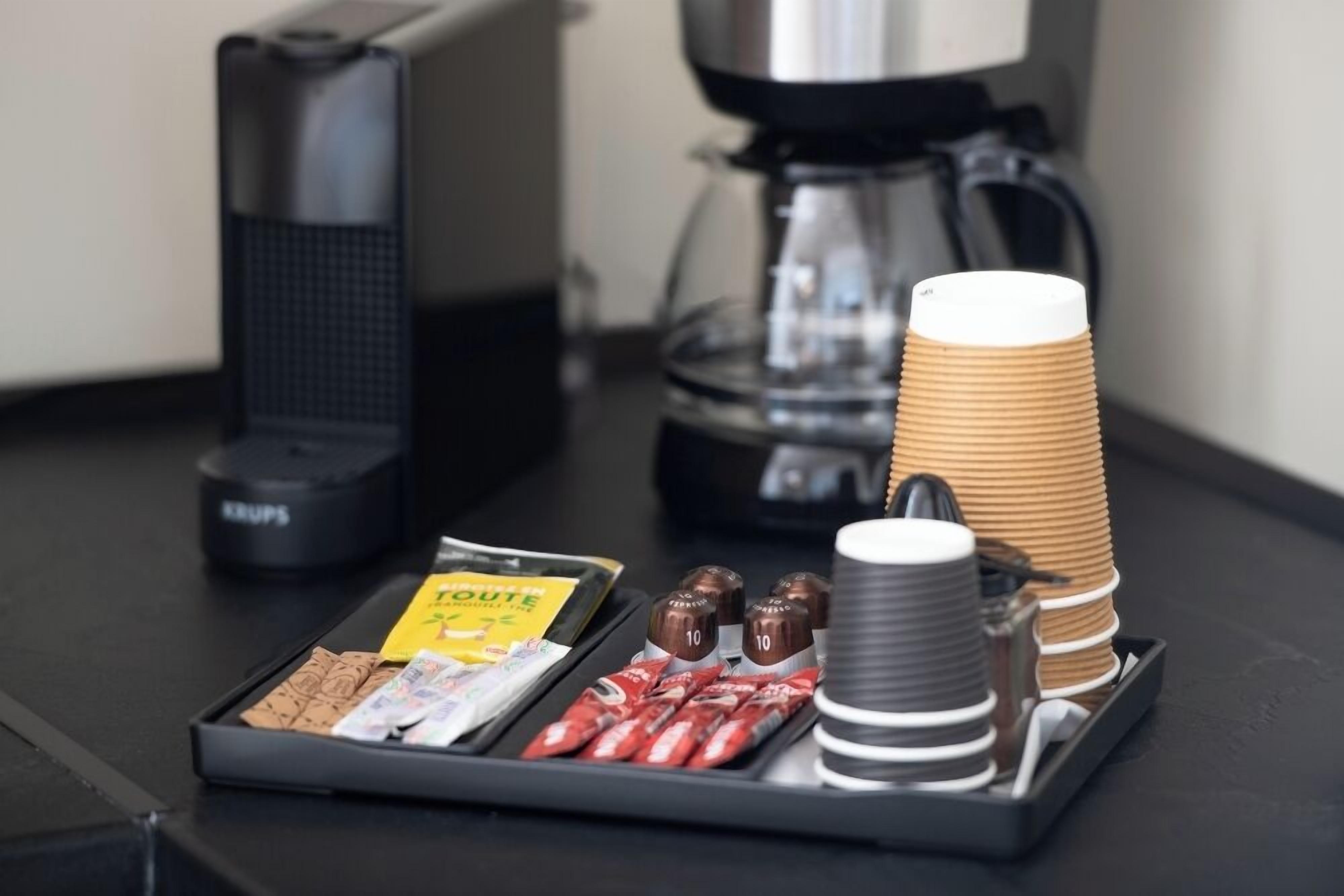 Un plateau avec une machine à café, une pile de gobelets en papier et quelques en-cas.