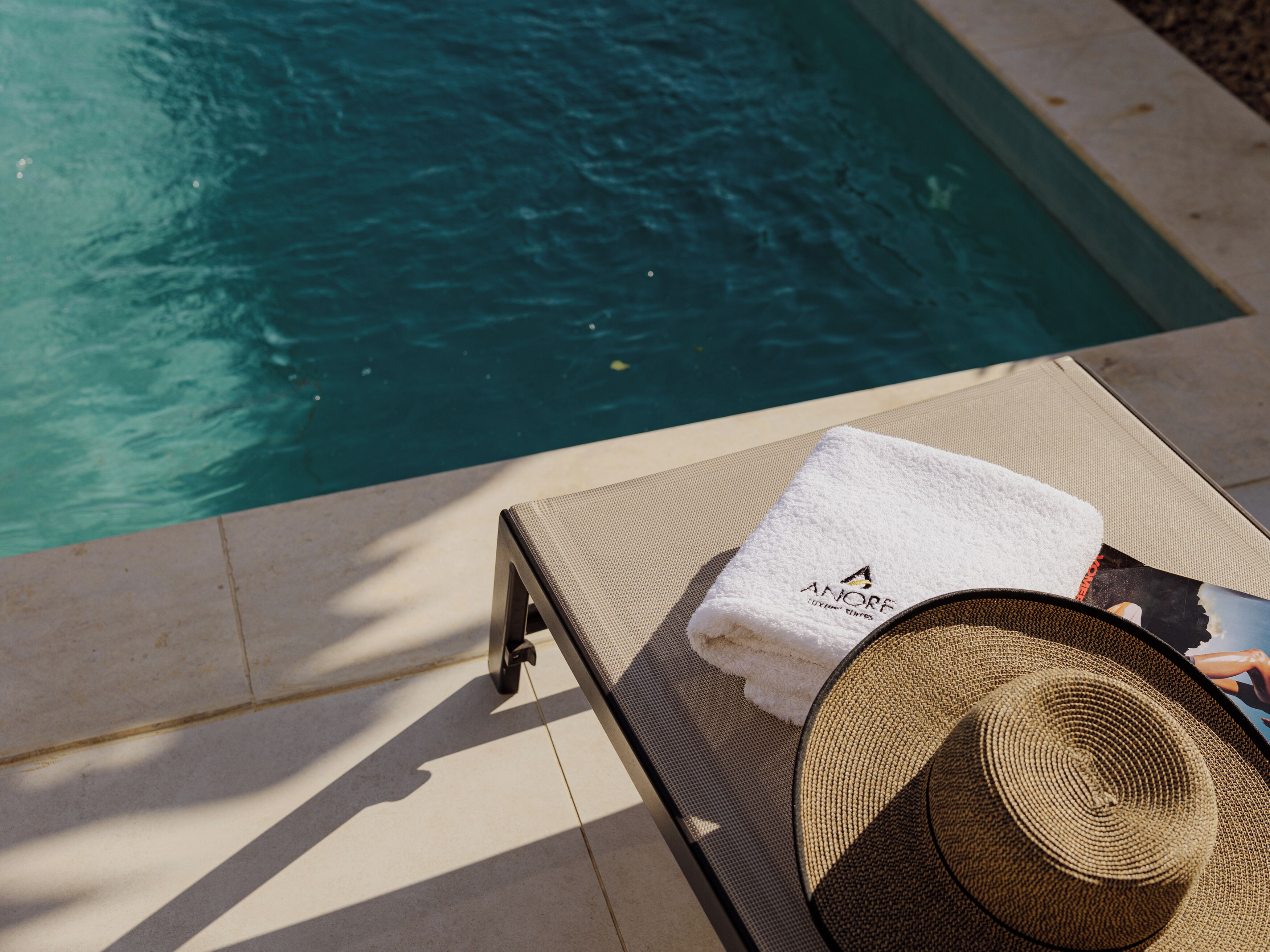 Una silla de descanso junto a la piscina con una toalla blanca y un sombrero de paja.
