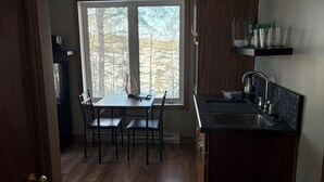Une cuisine équipée d’une table à manger, de chaises, d’une fenêtre donnant sur les arbres et d’un évier encastré.