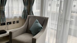 Un salon moderne avec un fauteuil gris, une petite table et un ordinateur portable. On y trouve des rideaux, une fenêtre et une vue sur l’extérieur.