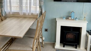 Une pièce chaleureuse avec une table et des chaises en bois, une cheminée, un téléviseur à écran plat et une fenêtre avec des rideaux.