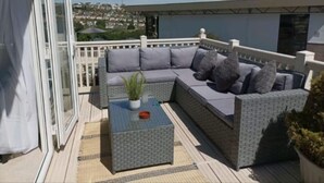 Un balcon avec un canapé d’angle gris, une petite table sur laquelle est posée une plante, et une vue sur le paysage urbain.