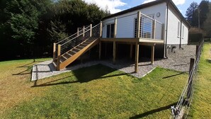 Uma casa moderna de dois andares, com um deck de madeira e uma escadaria que leva a uma área coberta.