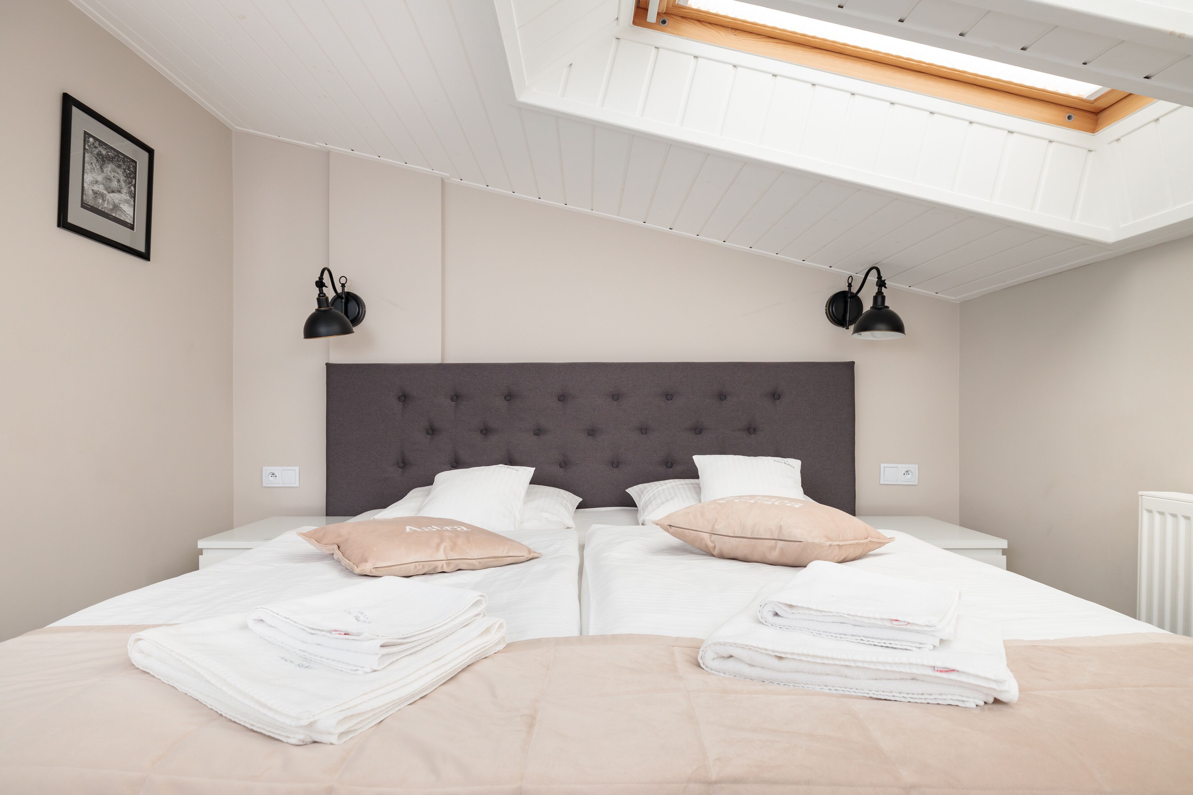 A bedroom with two beds, a skylight, and two wall-mounted lamps.