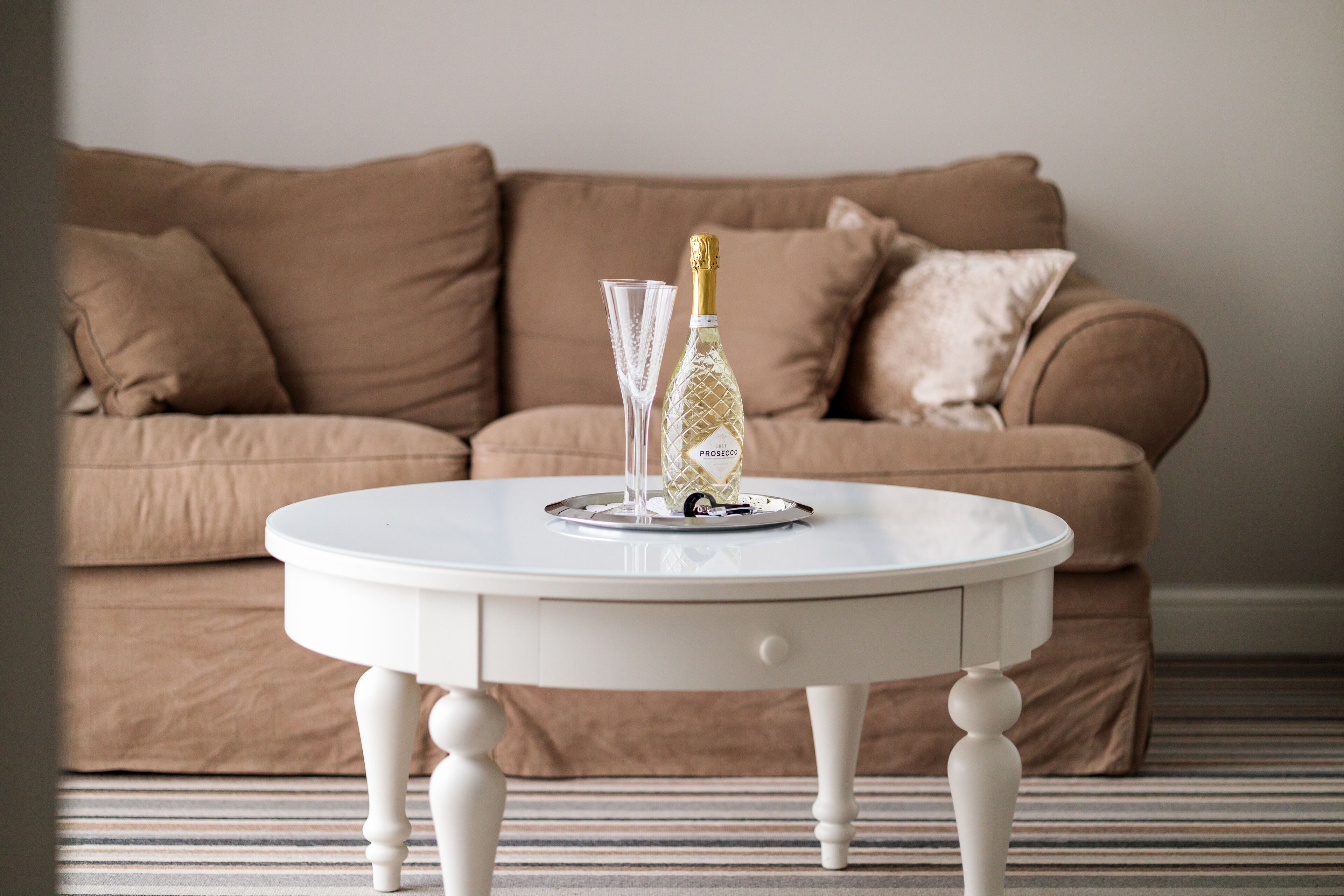 A white round table with a bottle and a glass in front of a brown sofa.