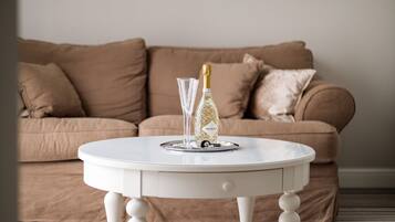 A white round table with a bottle and a glass in front of a brown sofa.