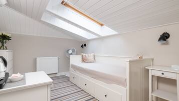 Un dormitorio con una cama, un escritorio, un radiador, un ventilador y un tragaluz.